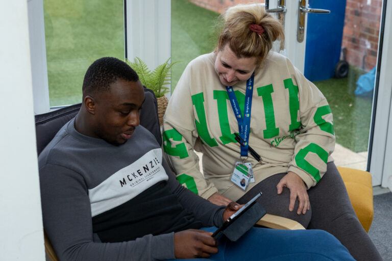 Carer and adult we support sat looking at ipad having a conversation.